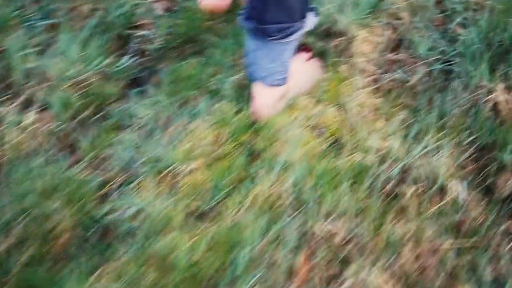 Blurry image of bare feet in rolled up jeans walking through grass