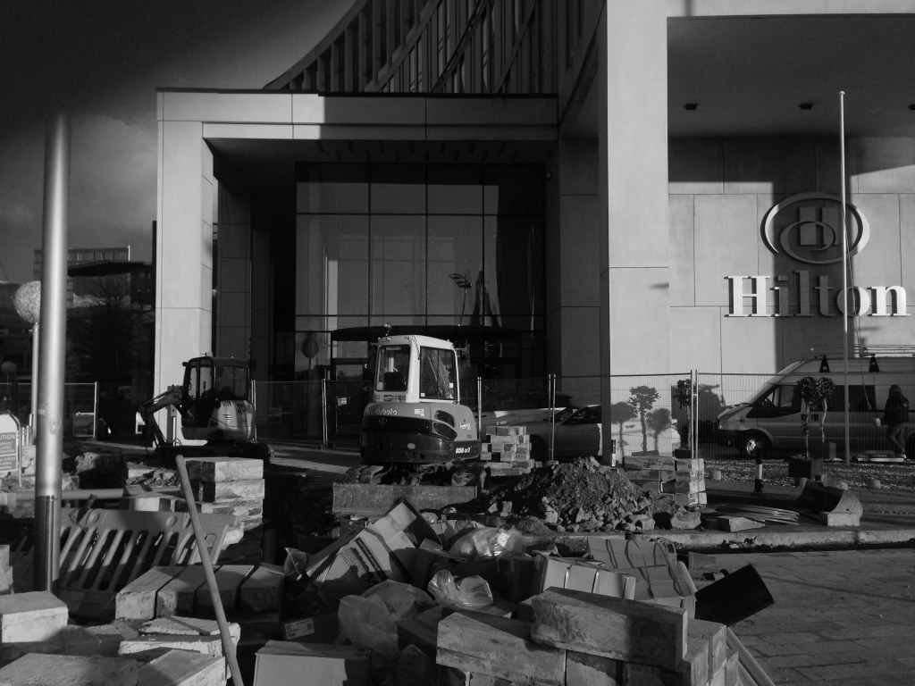 Hilton hotel entrance with dug up concrete slabs and diggers in exterior doorway, in black and white 